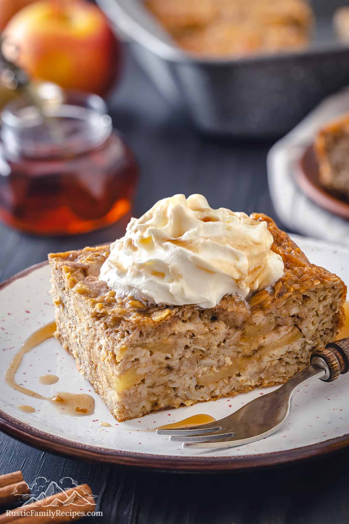 Slice of baked oatmeal on a white plate with maple syrup and whipped cream
