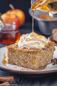 Pouring maple syrup onto a slice of baked apple oatmeal with whipped cream