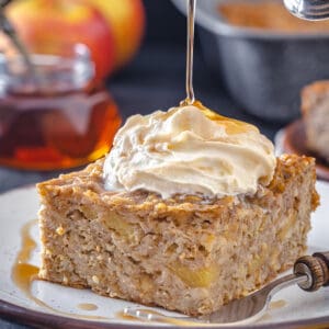 Pouring maple syrup onto a slice of baked apple oatmeal with whipped cream