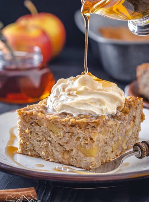 Pouring maple syrup onto a slice of baked apple oatmeal with whipped cream