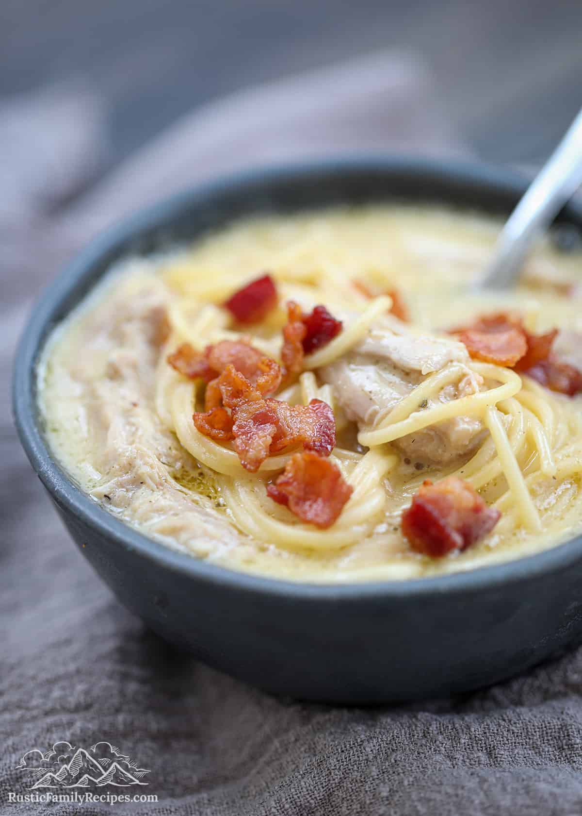 This Crack Chicken Noodle Soup recipe is everything you want in a bowl of soup. Made with tender chicken, noodles, and BIG flavor! A grey bowl filled with crack chicken noodle soup, with a spoon in the bowl