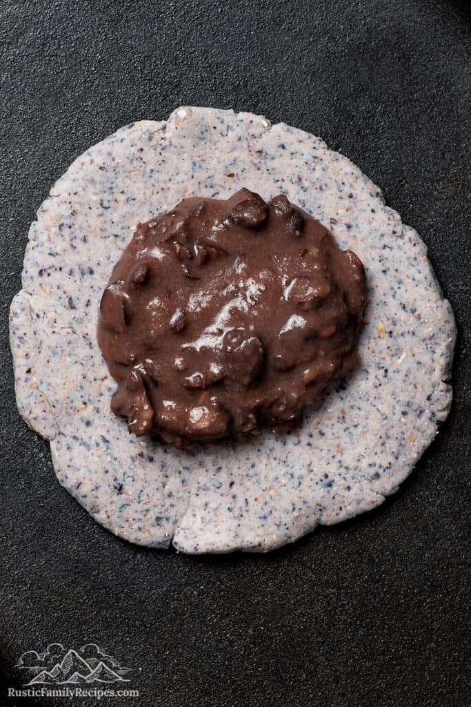 Adding refried beans to the center of the flattened dough.