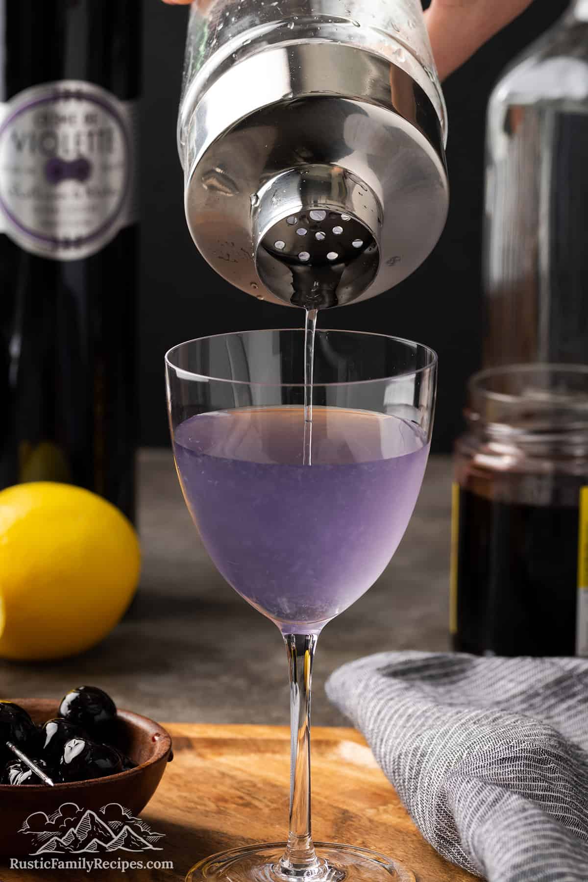Pouring an Aviation Cocktail from a cocktail shaker into a glass
