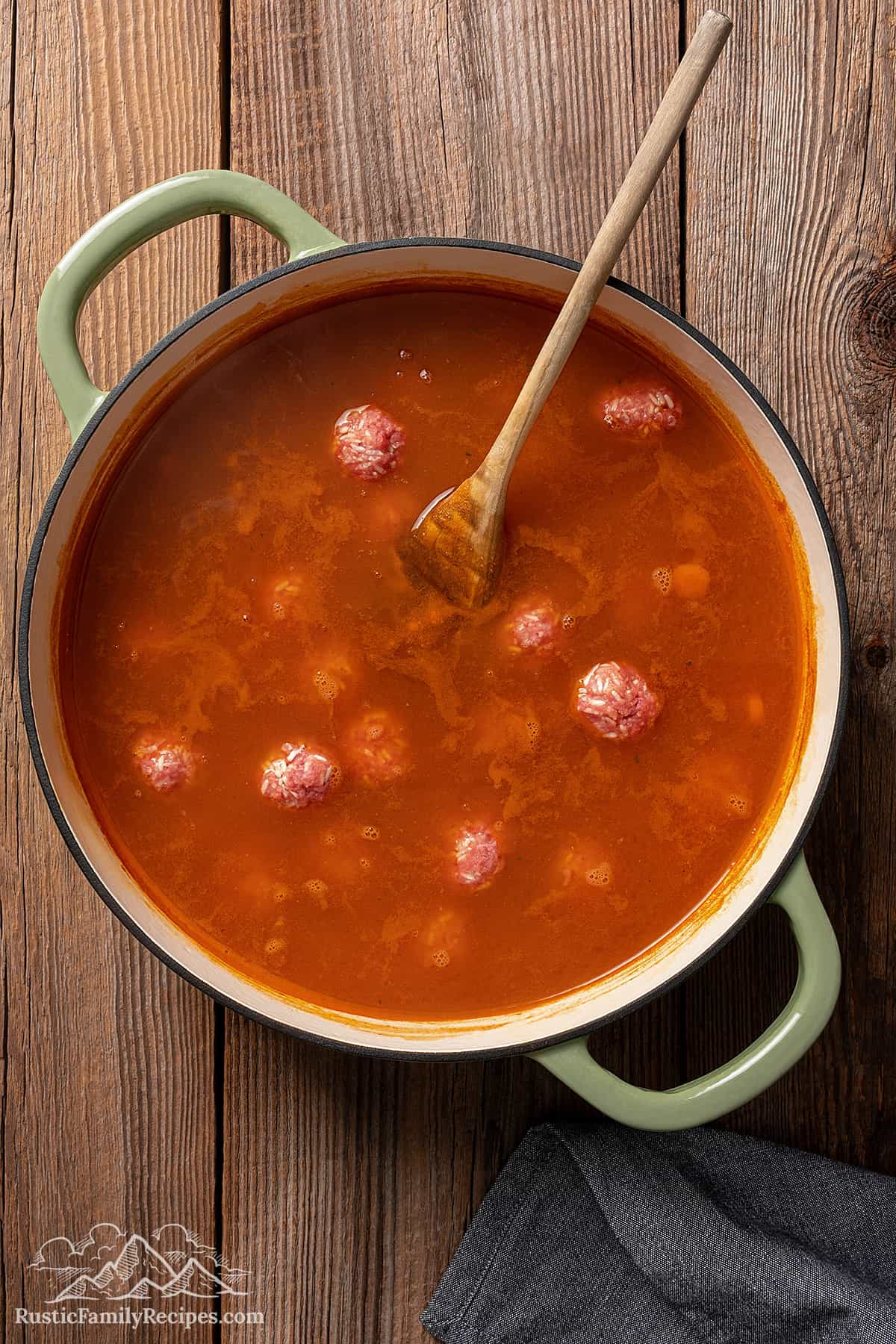 Adding meatballs to cook in a pot with tomato broth