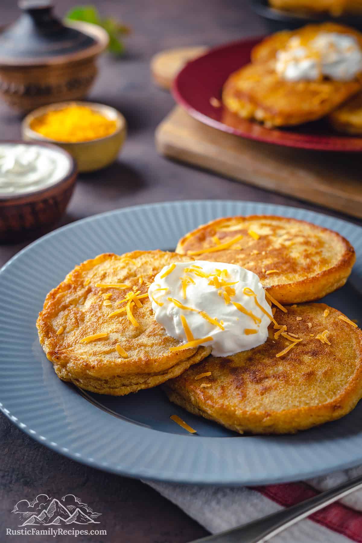 Three hot cakes on a plate with sour cream and cheese on top