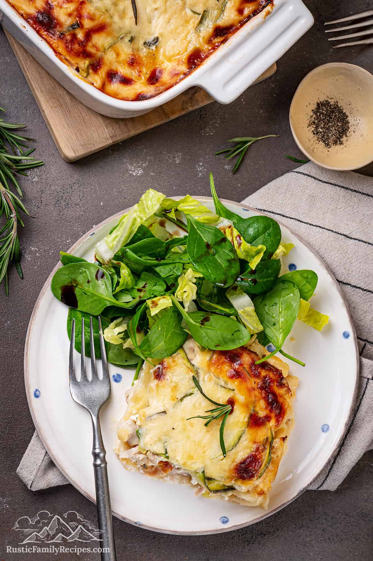 A slice of Roasted Chicken Bechamel Lasagna on a white plate with a fork and salad