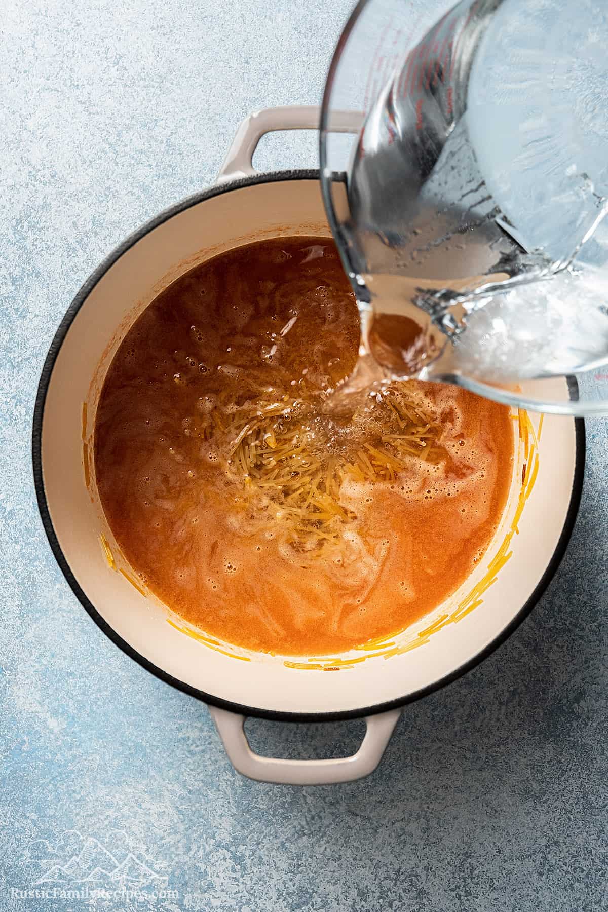 Adding water to a pot with tomato broth and fideos