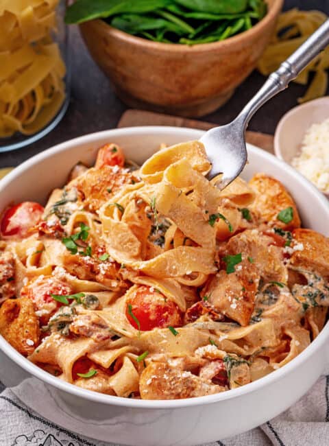 Tuscan chicken pasta served in a bowl with a fork and spoon
