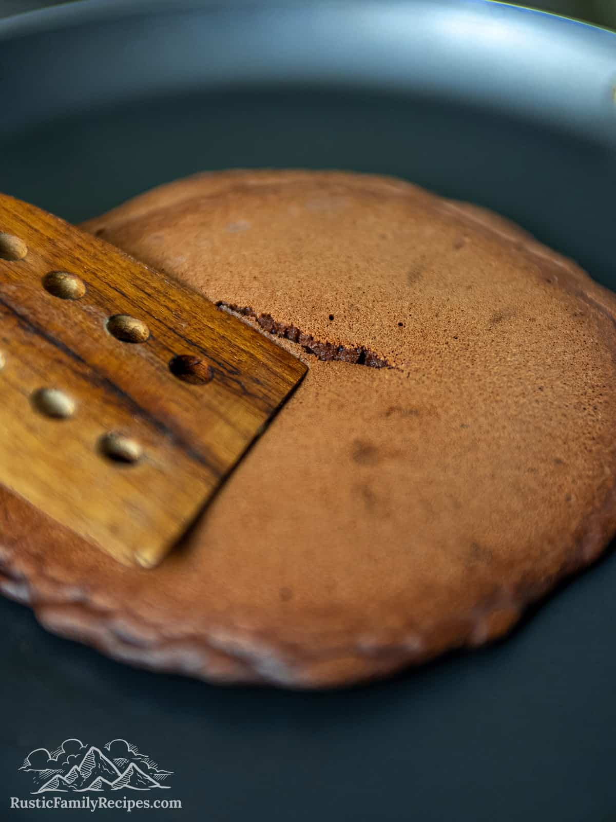 A wood spatula making a small crack in a chocolate pancake