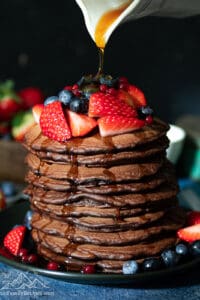A stack of chocolate pancakes with syrup being poured on top