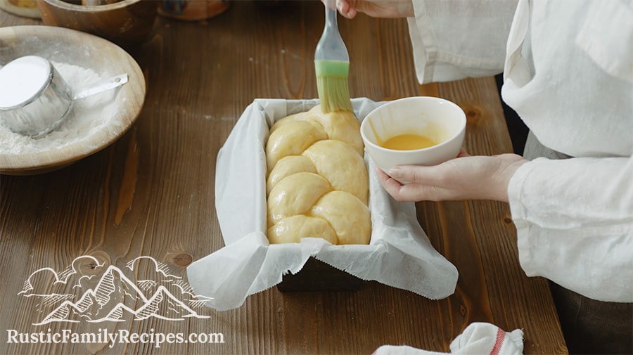 Adding egg wash to challah dough in a loaf pan