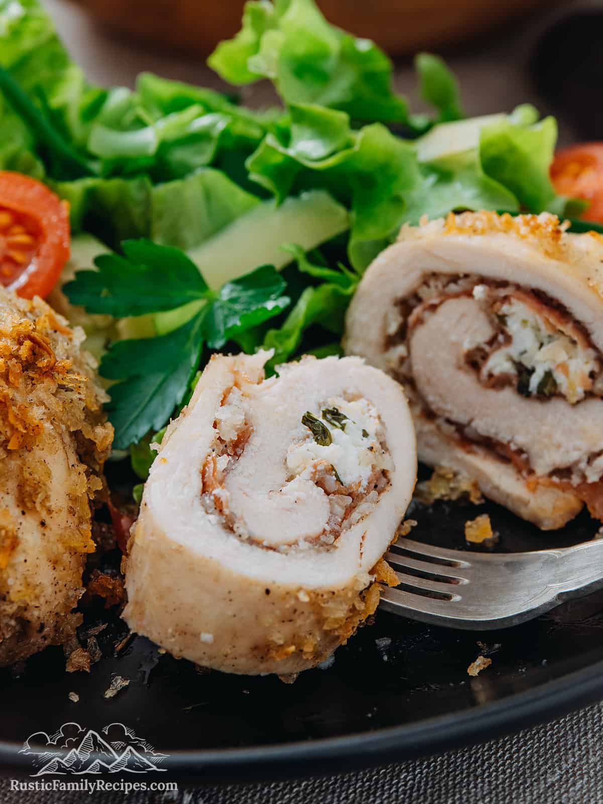 This easy chicken rollatini recipe is made with breaded chicken cutlets rolled around prosciutto and a creamy herbed ricotta filling. Cut open chicken rollatini on a plate with salad