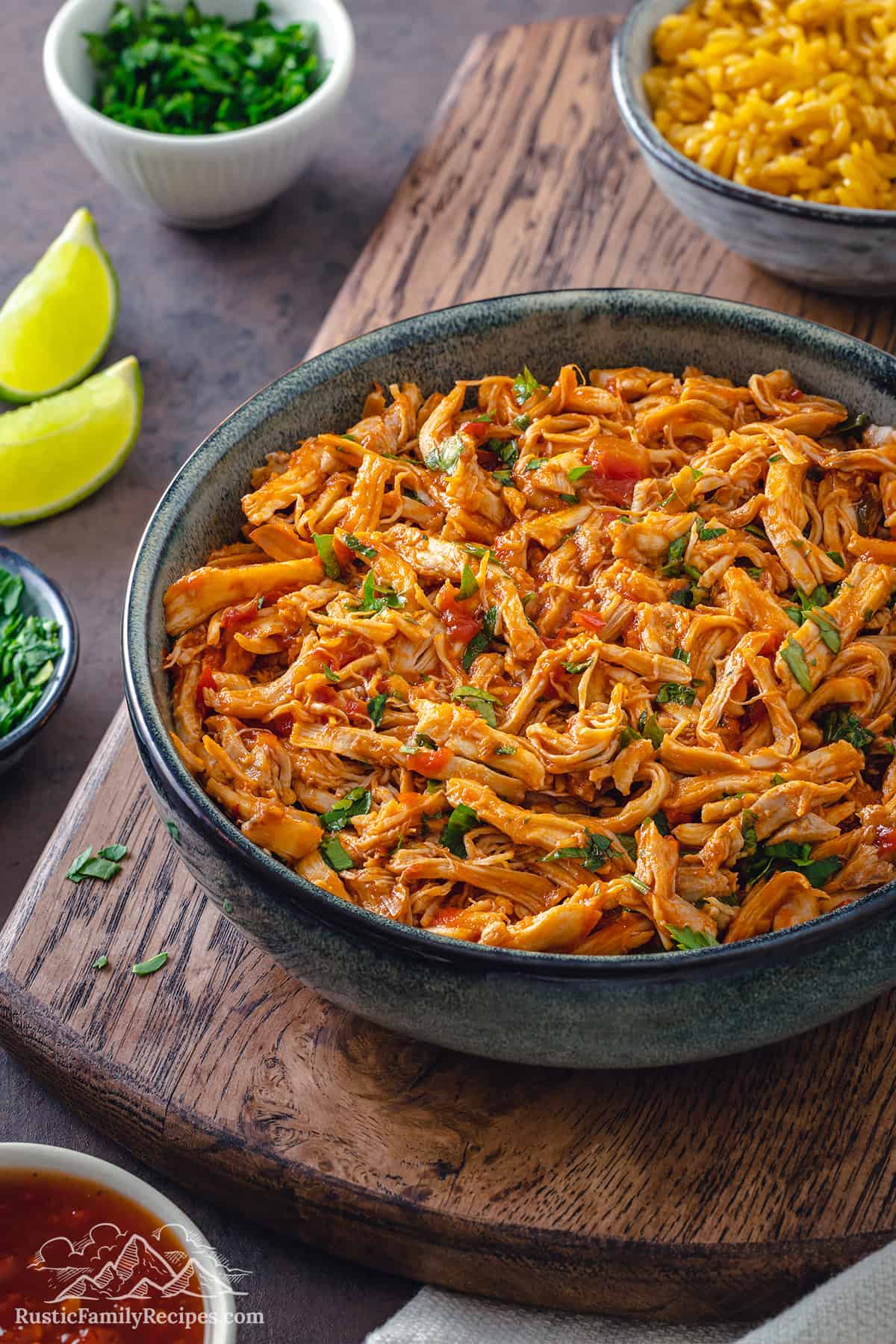 A bowl filled with salsa shredded chicken with a fork and lime wedges