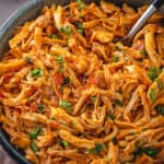 A bowl filled with salsa shredded chicken with a fork and lime wedges