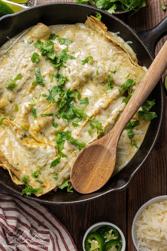 Enchiladas suizas in the skillet with a wooden spoon on top.