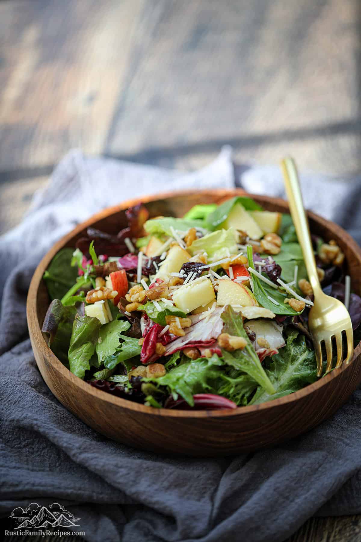 A wood bowl filled with spring mix salad, a gold fork in the bowl