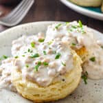 A cathead biscuit cut in half, smothered in gravy, and garnished with fresh parsley on a plate.