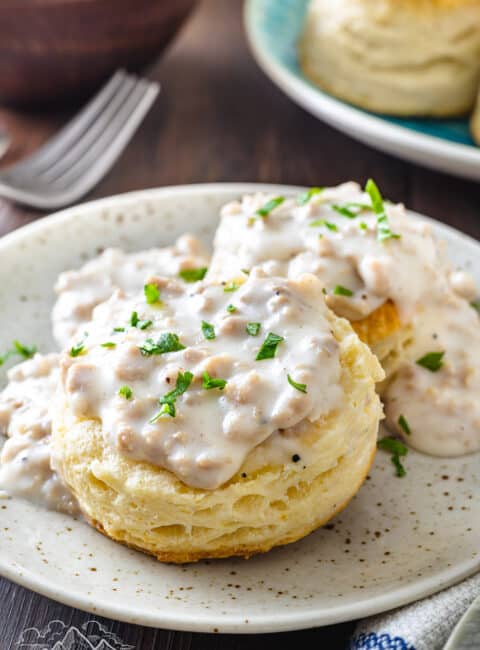 A cathead biscuit cut in half, smothered in gravy, and garnished with fresh parsley on a plate.