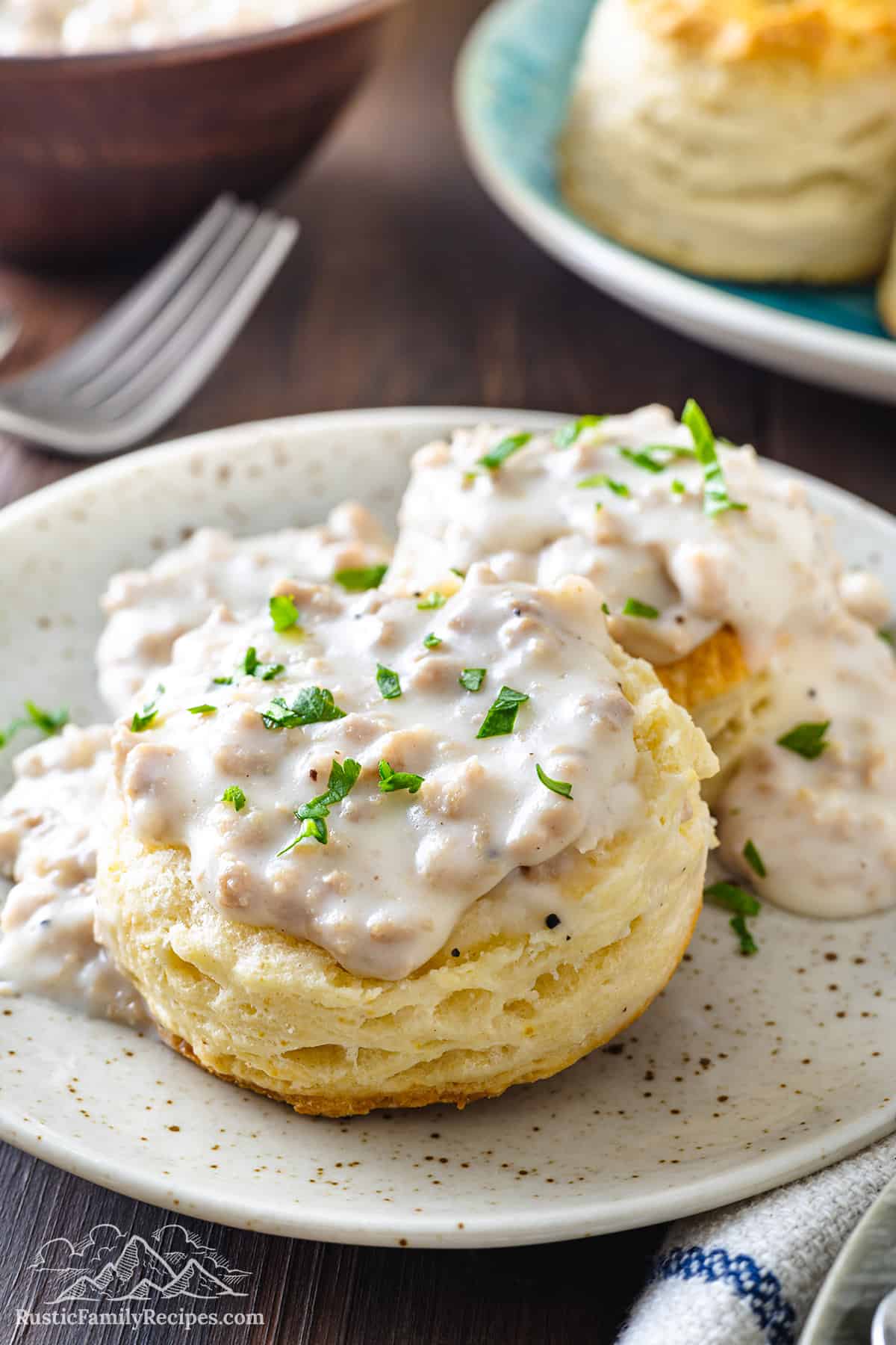 A cathead biscuit cut in half, smothered in gravy, and garnished with fresh parsley on a plate.