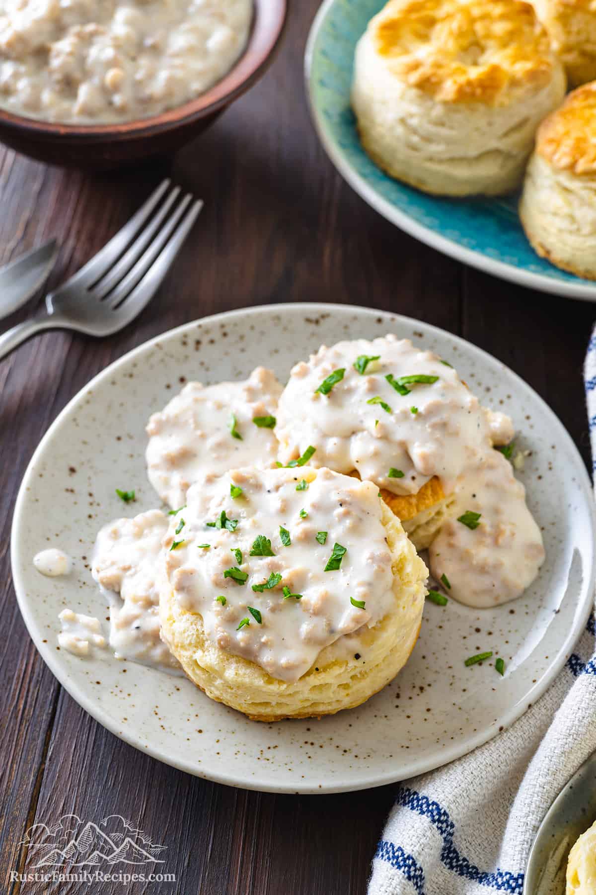 Two cathead biscuits smothered in gravy and garnished with fresh parsley on a plate.