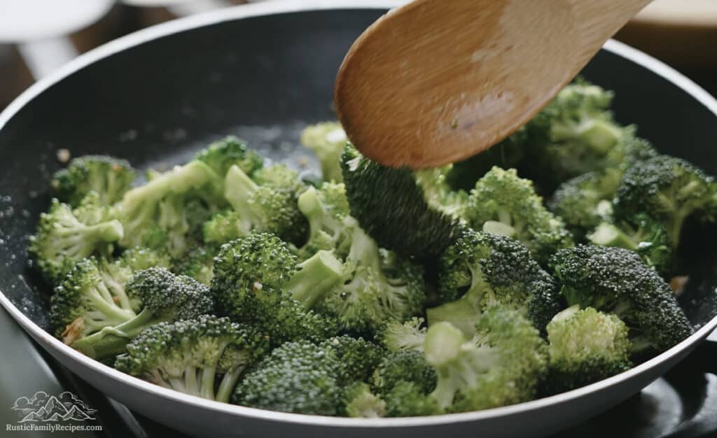 Cooking broccoli in a pan with a wooden spoon