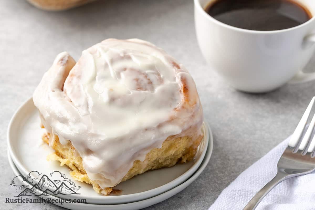 A cinnamon bun on a plate next to a cup of coffee
