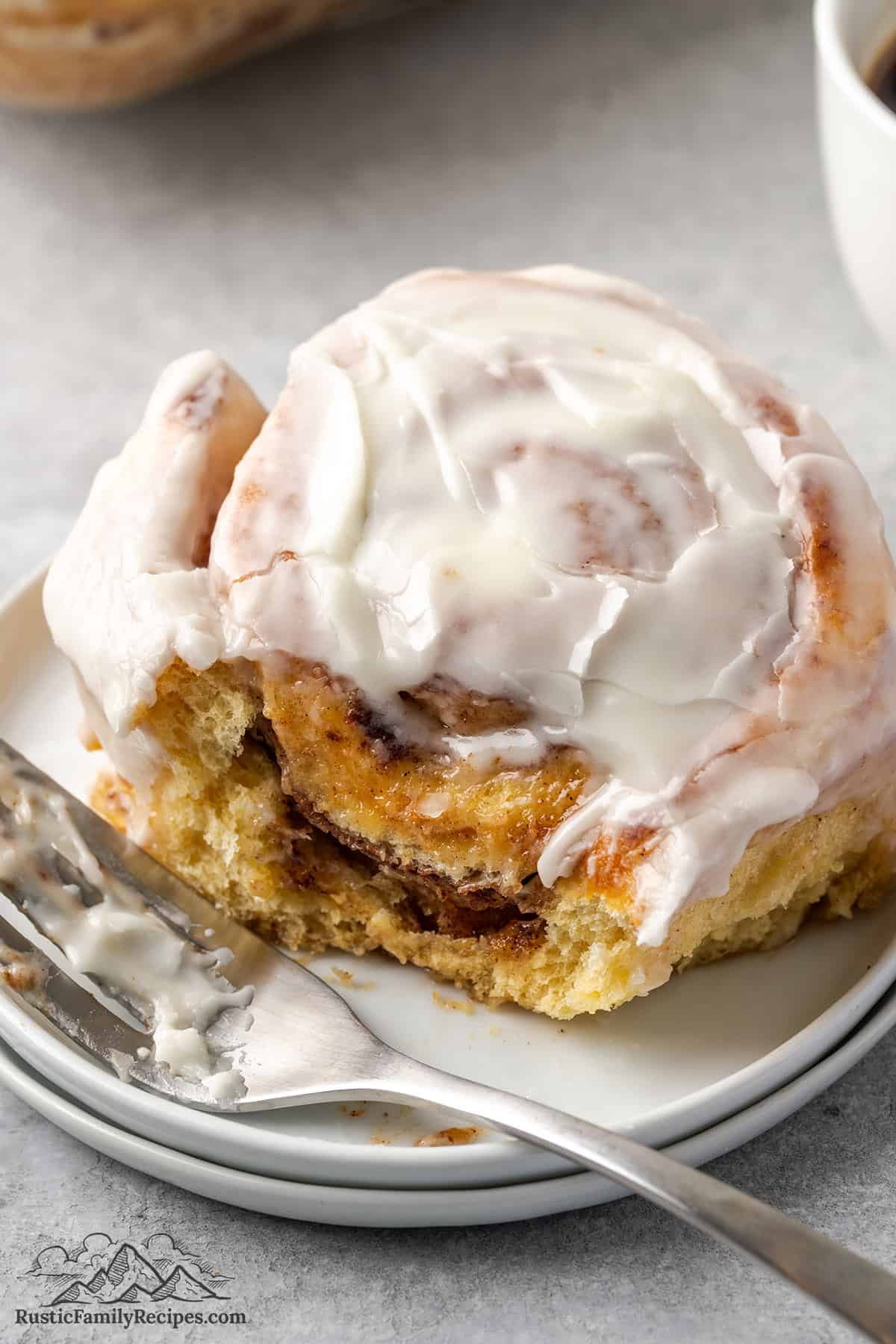 A cinnamon bun on a plate with a fork, a bite taken out