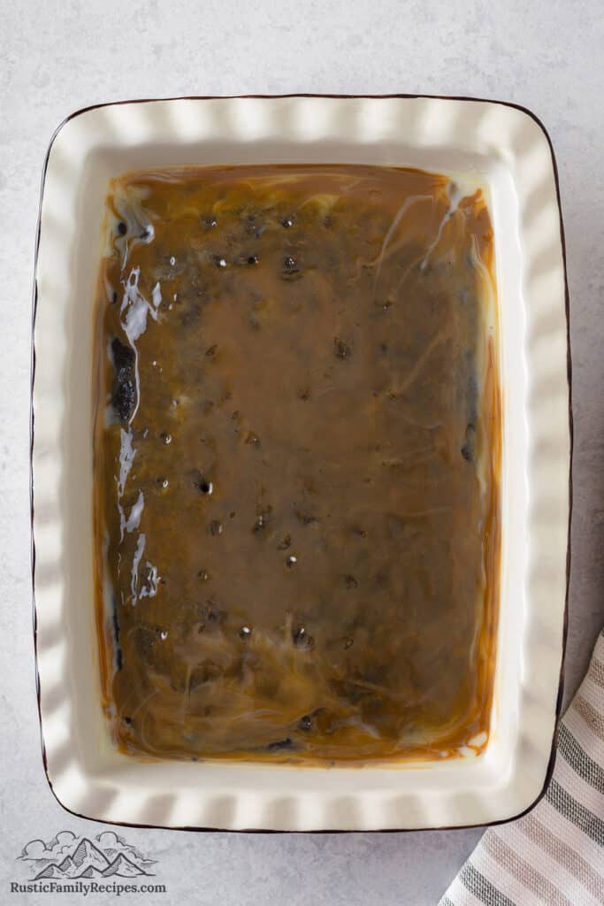 Adding caramel sauce to a chocolate cake with holes poked into it