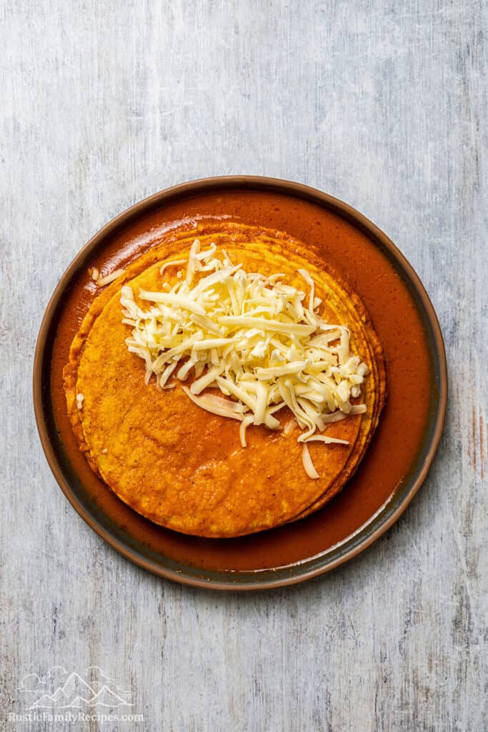 Tortillas dipped in sauce topped with chicken birria and shredded cheese.