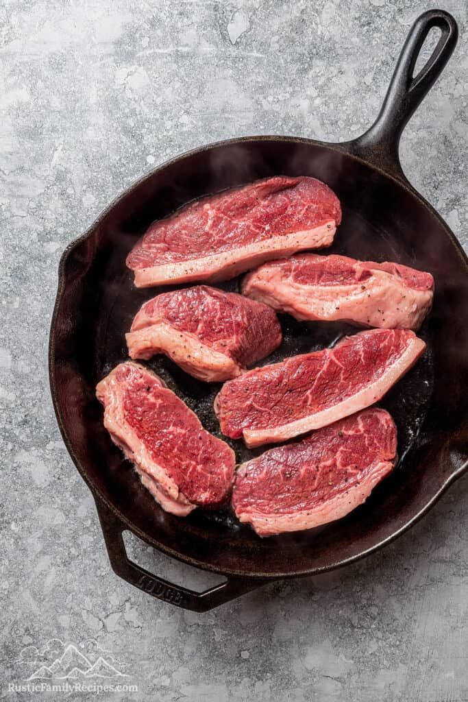 Six steak fillets in a large cast-iron skillet.