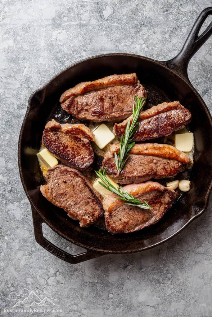 Butter, garlic, and rosemary added to a skillet with seared coulotte steaks.