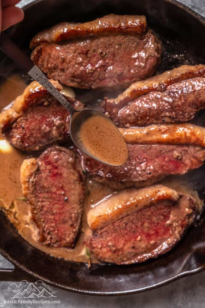 Melted butter is spooned over coulotte steaks as they cook in a cast iron skillet.