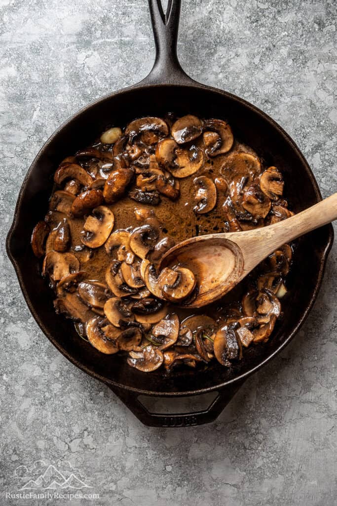 Buttery mushroom sauce in a skillet with a wooden spoon.