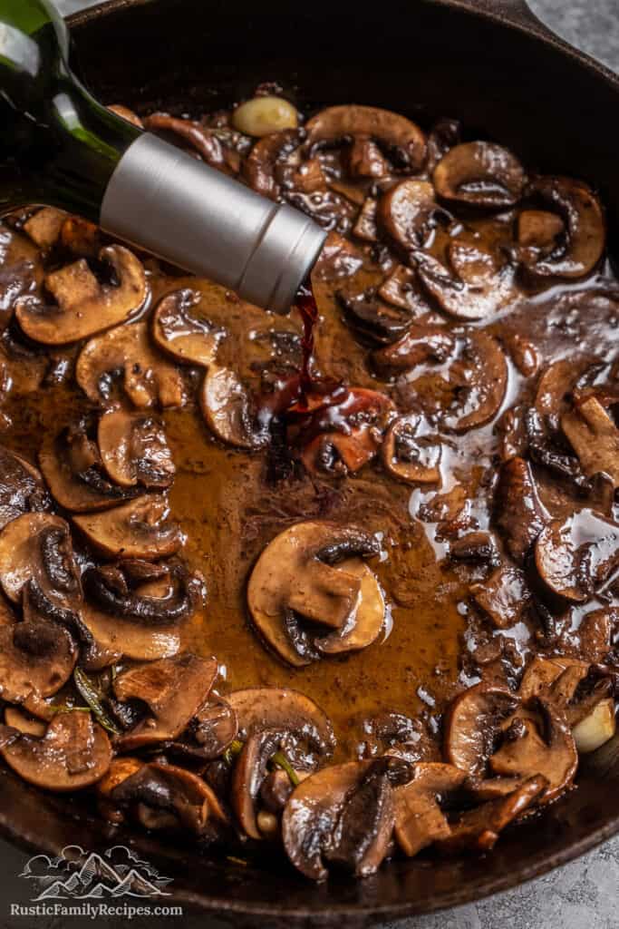 Red wine is poured into mushroom sauce in a skillet.
