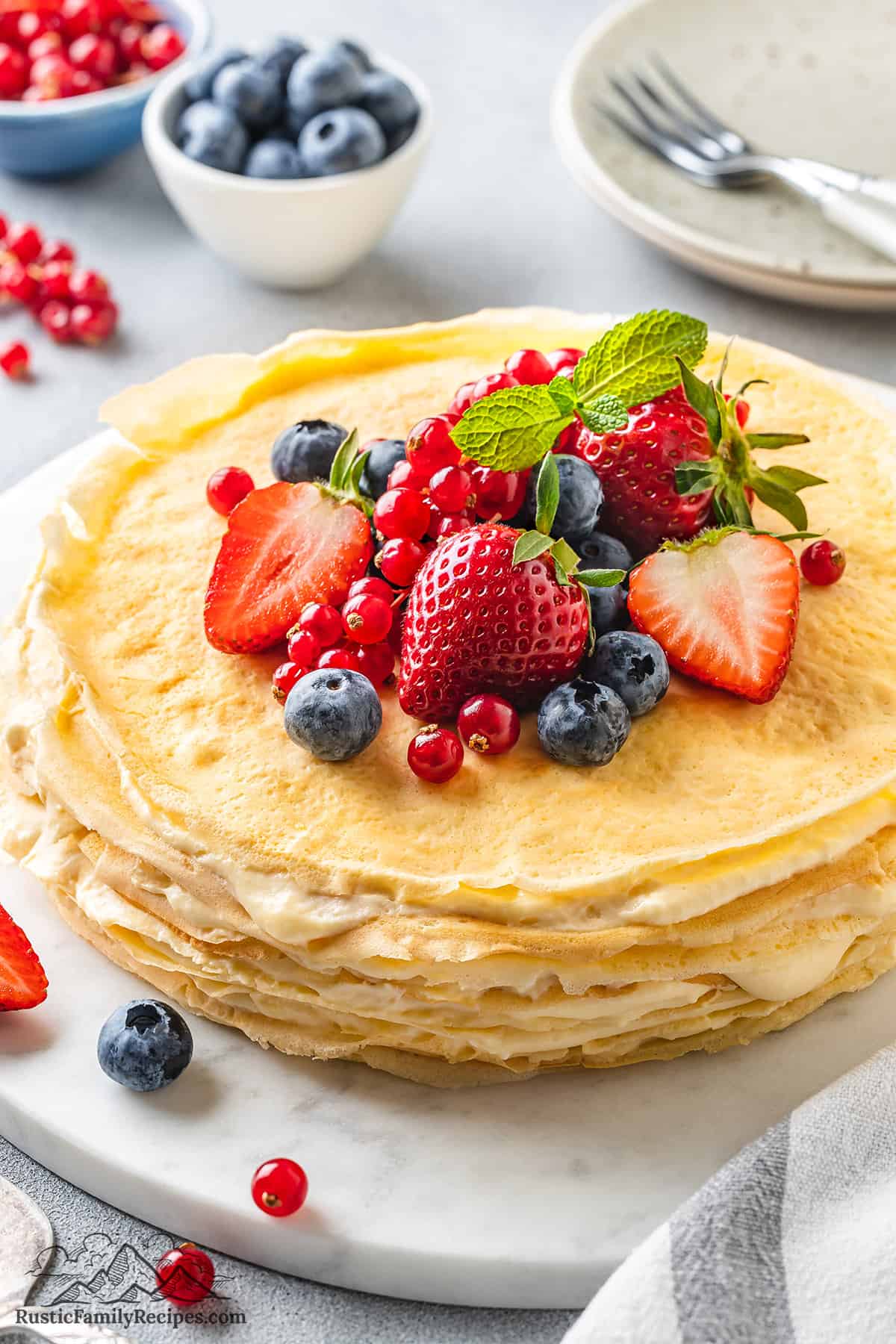 A crepe cake on a platter with fruit in the background