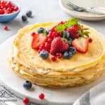 A crepe cake on a platter with fruit in the background