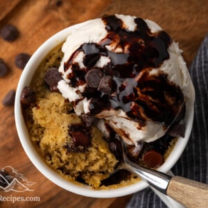 Top view of a chocolate chip cookie in a mug with ice cream and chocolate sauce.