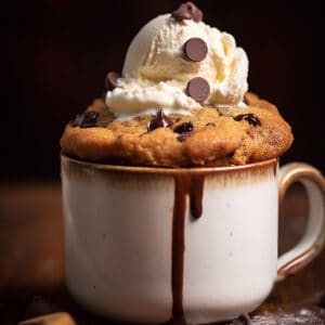 A rustic mug with a chocolate chip cookie in it topped with ice cream