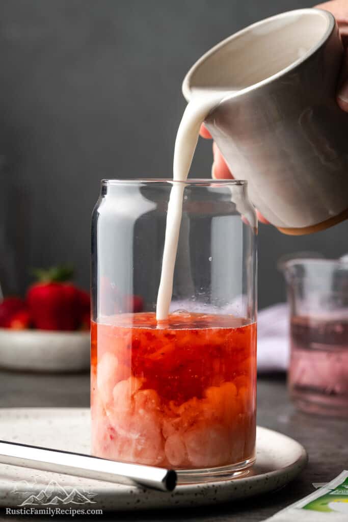 Pouring coconut milk into a glass with mashed strawberries
