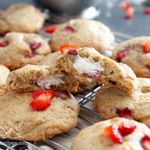 A pile of strawberry cheesecake stuffed cookies with one cookie broken in half to show the filling.