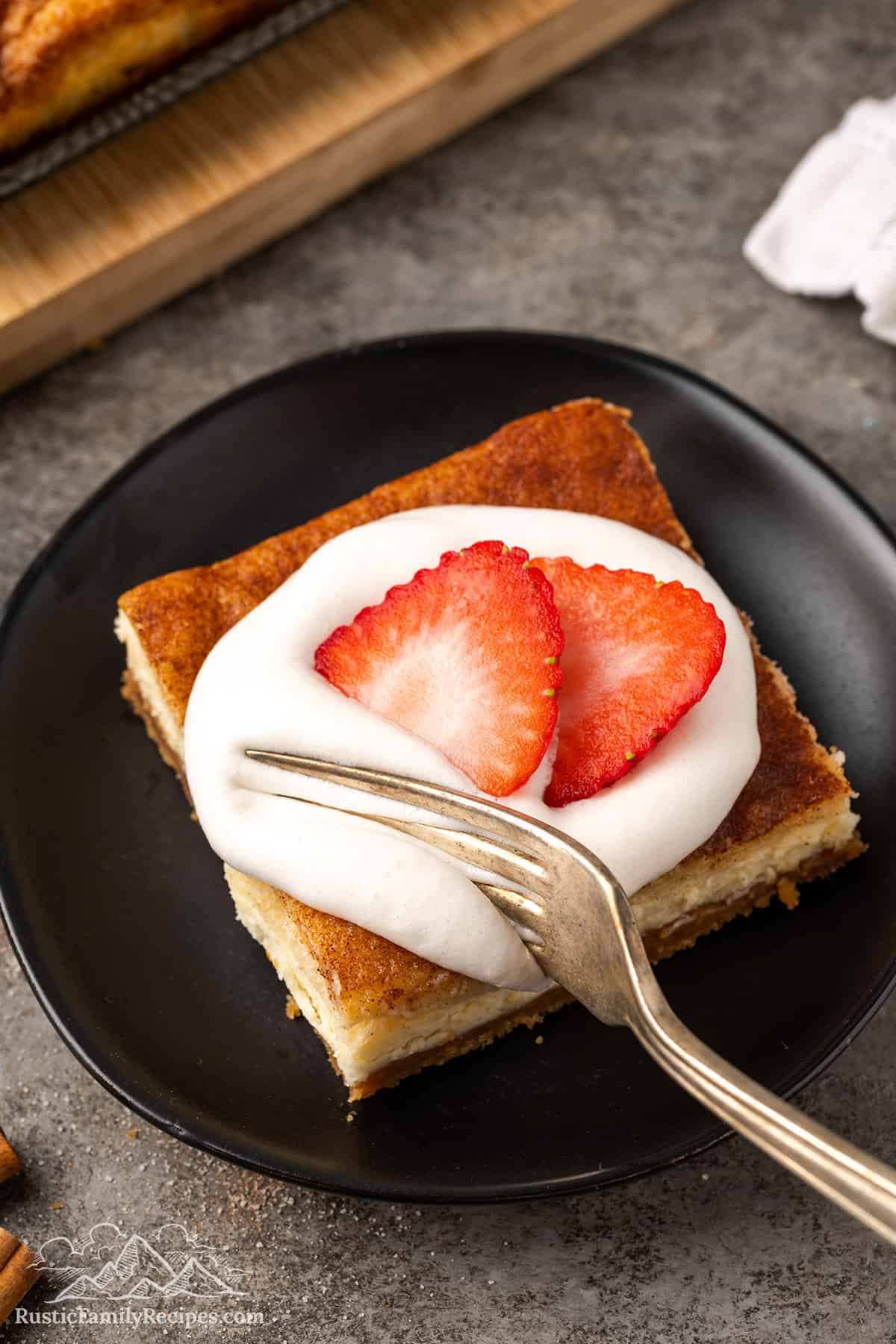 A fork taking a slice of churro cheesecake topped with whipped cream and strawberry slices