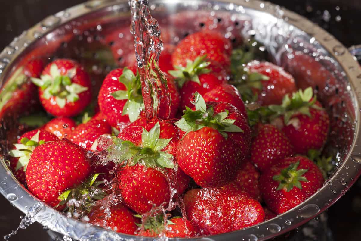 Running water over strawberries in a colander.