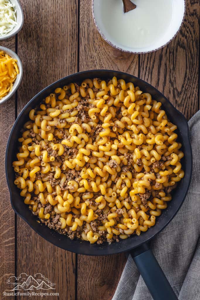 Pasta added to a skillet with seasoned ground beef.