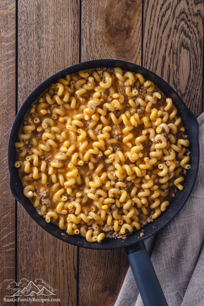 Cooked pasta combined with ground beef and cheese in a cast iron skillet.