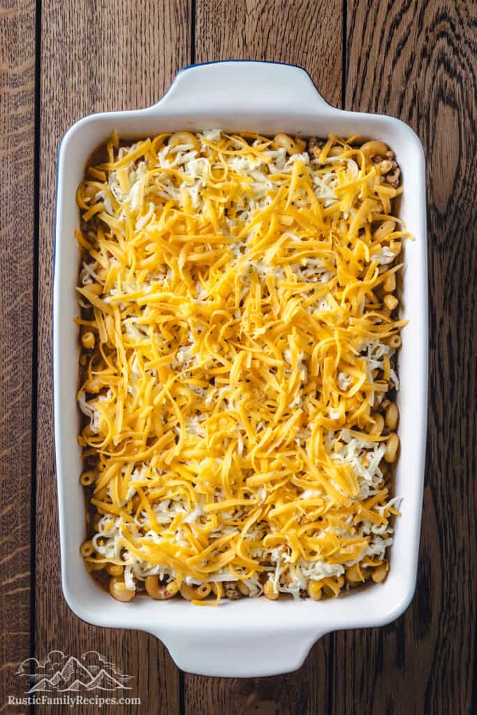 Assembled cheeseburger casserole in a 9x13 casserole dish, topped with shredded cheese.