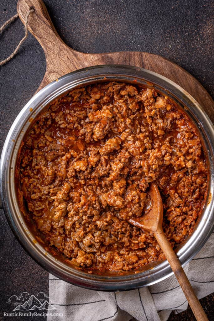 Meat sauce in a large pan with a wooden spoon.