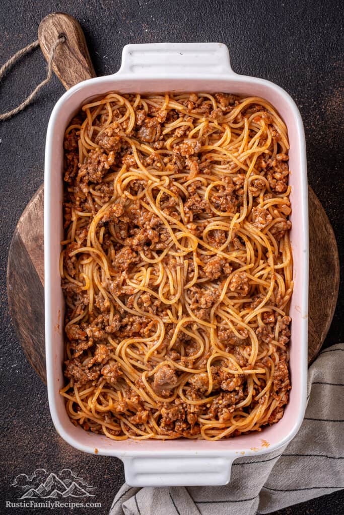 Spaghetti tossed with meat sauce spread into a casserole dish.