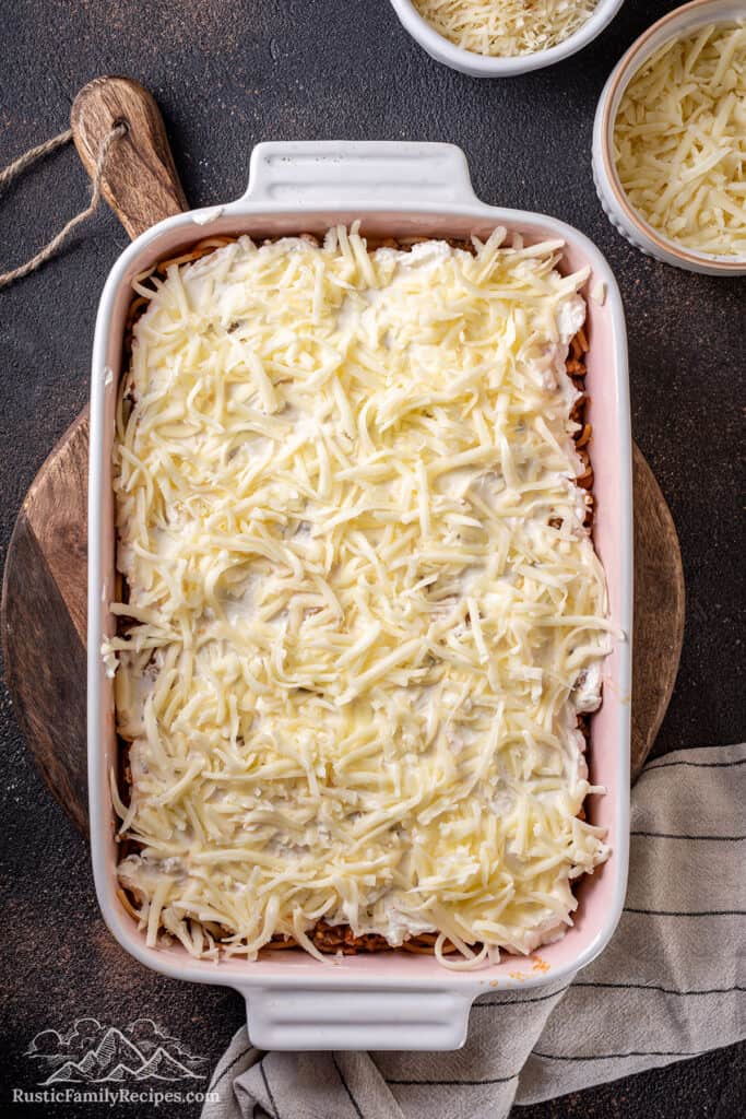 Cheese layered over spaghetti tossed with meat sauce in a casserole dish.
