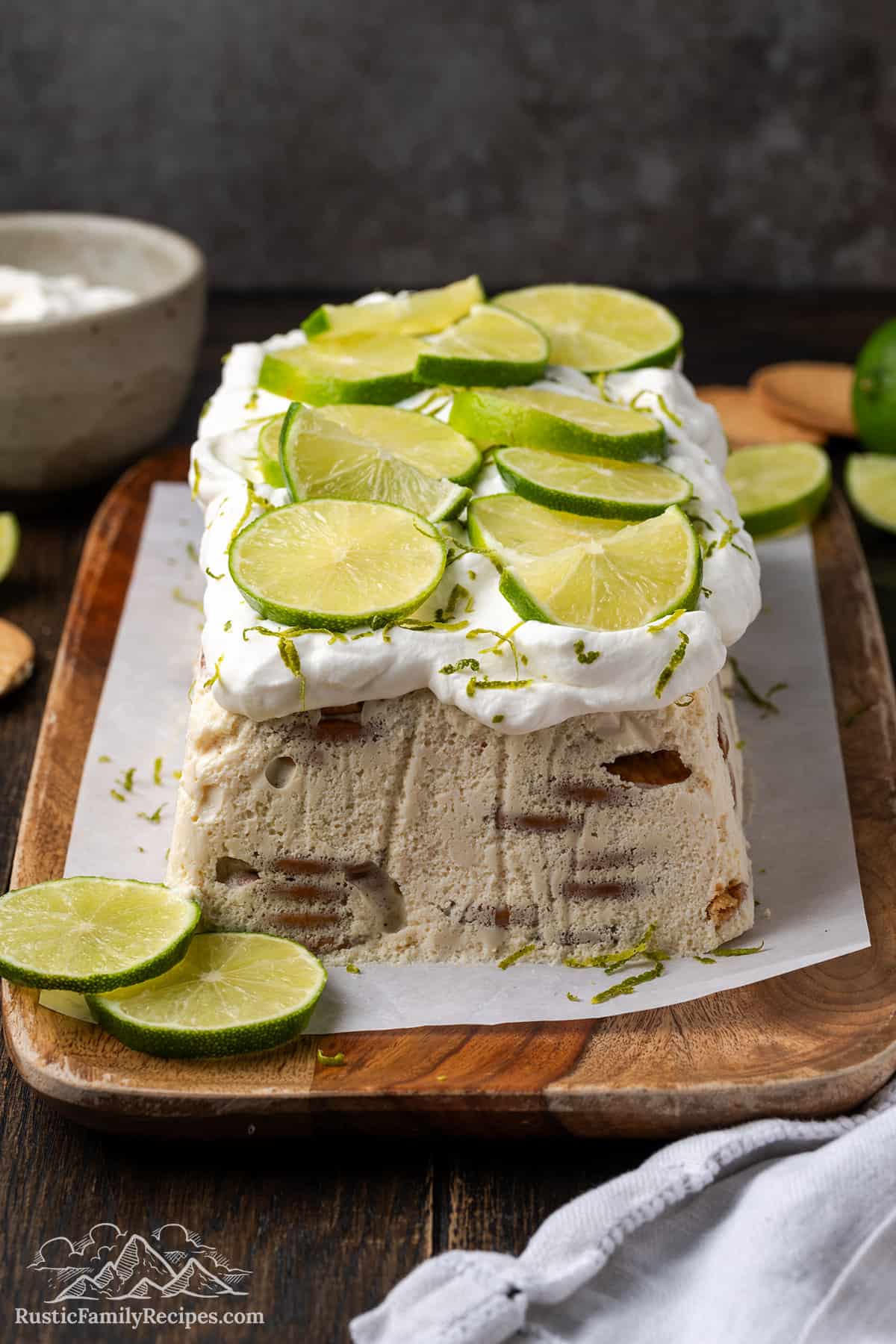 A carlota de limon icebox cake on a cutting board, topped with whipped cream and thinly sliced limes.