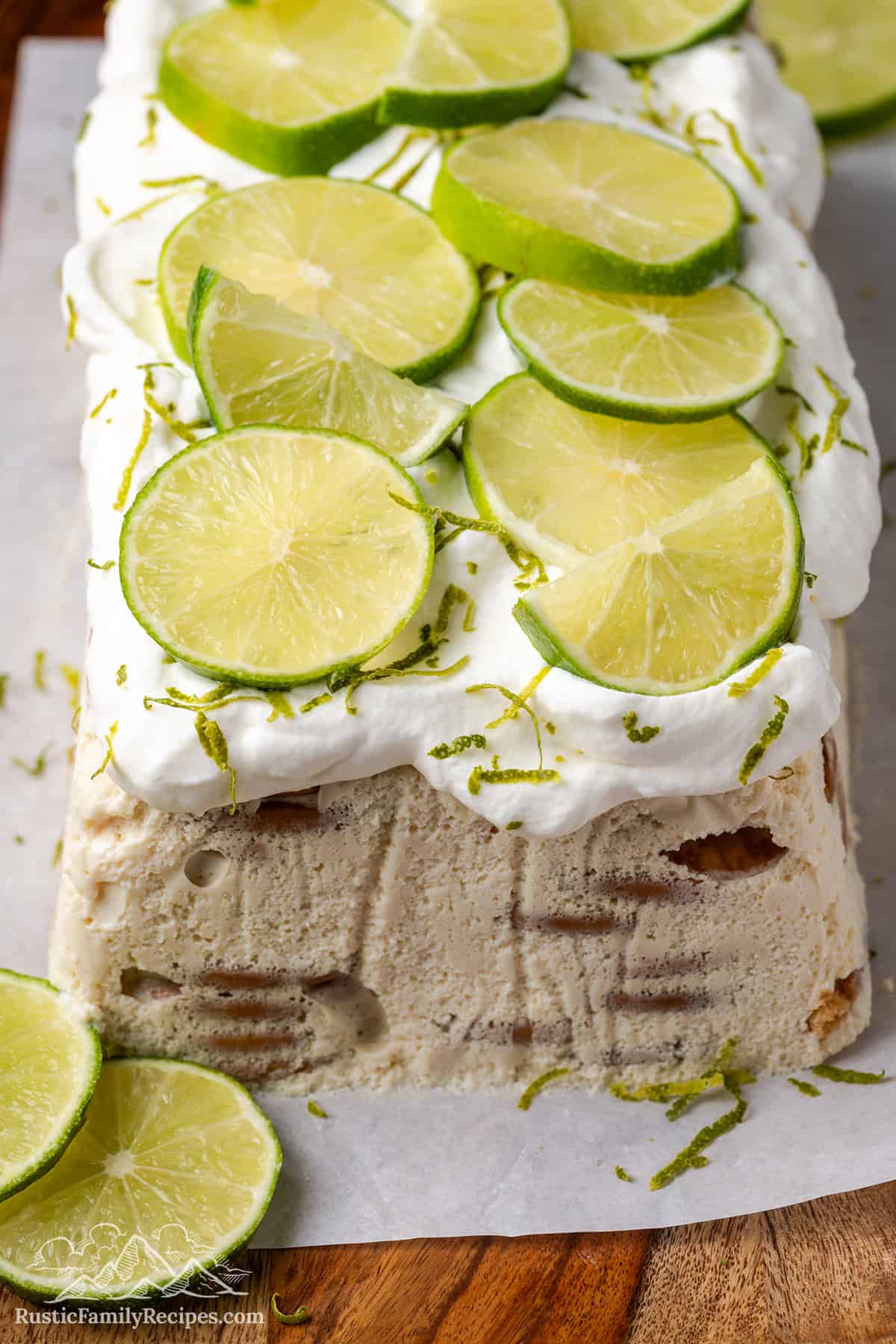 Close up of a carlota de limon icebox cake on a cutting board, topped with whipped cream and thinly sliced limes.